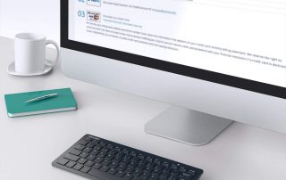 Escritorio moderno con ordenador Mac una taza blanca de cafe y una libreta verde. Teclado compacto y ratón inalámbricos en negro.