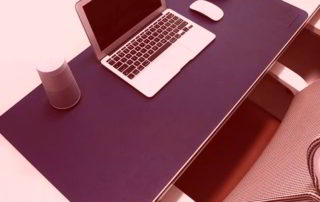 Alfombrilla grande azul sobre escritorio, con un portátil encima y un ratón, al lado se ve parte de una silla de oficina.