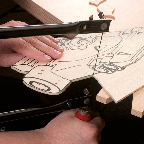 manos con una sierra de marquetería recortando una figura dibujada en una lámina de madera con forma de coche de formula uno.